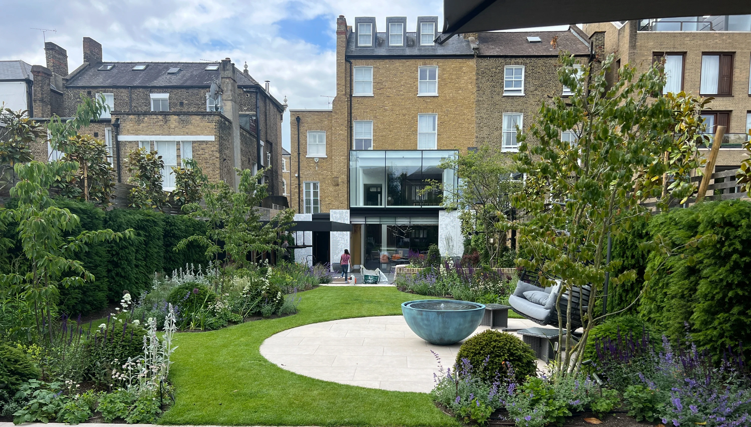 Contemporary courtyard garden with circular paving, water feature, lawn and layered planting designed by Flourish Landscaping